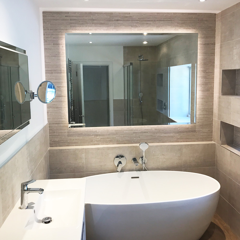 Modern bathroom with a large backlit mirror, an oval freestanding bathtub, a sink with chrome fixtures, and beige tiled walls.