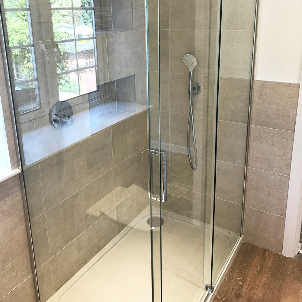 Glass-enclosed shower with beige tiled walls, a built-in bench under a window, and a handheld showerhead.