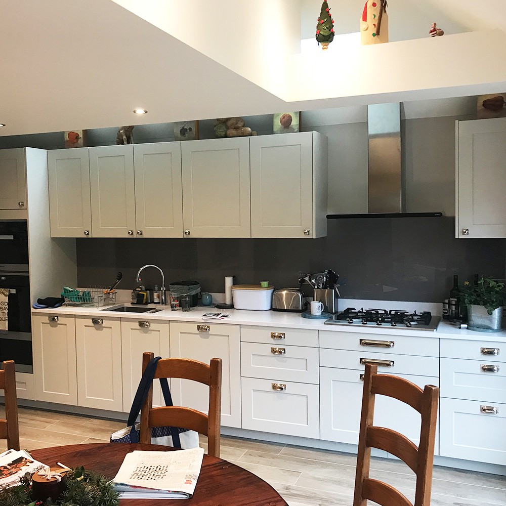 Modern kitchen with white cabinets, stainless steel appliances, a round wooden dining table with chairs, and various kitchen items on the counters and shelves.