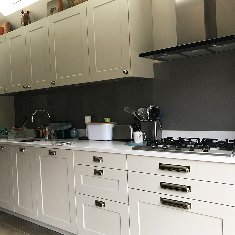 Modern kitchen with white cabinets, gas stove, utensils in holders, dishes near the sink, and small appliances on the countertop under a neutral-colored backsplash.