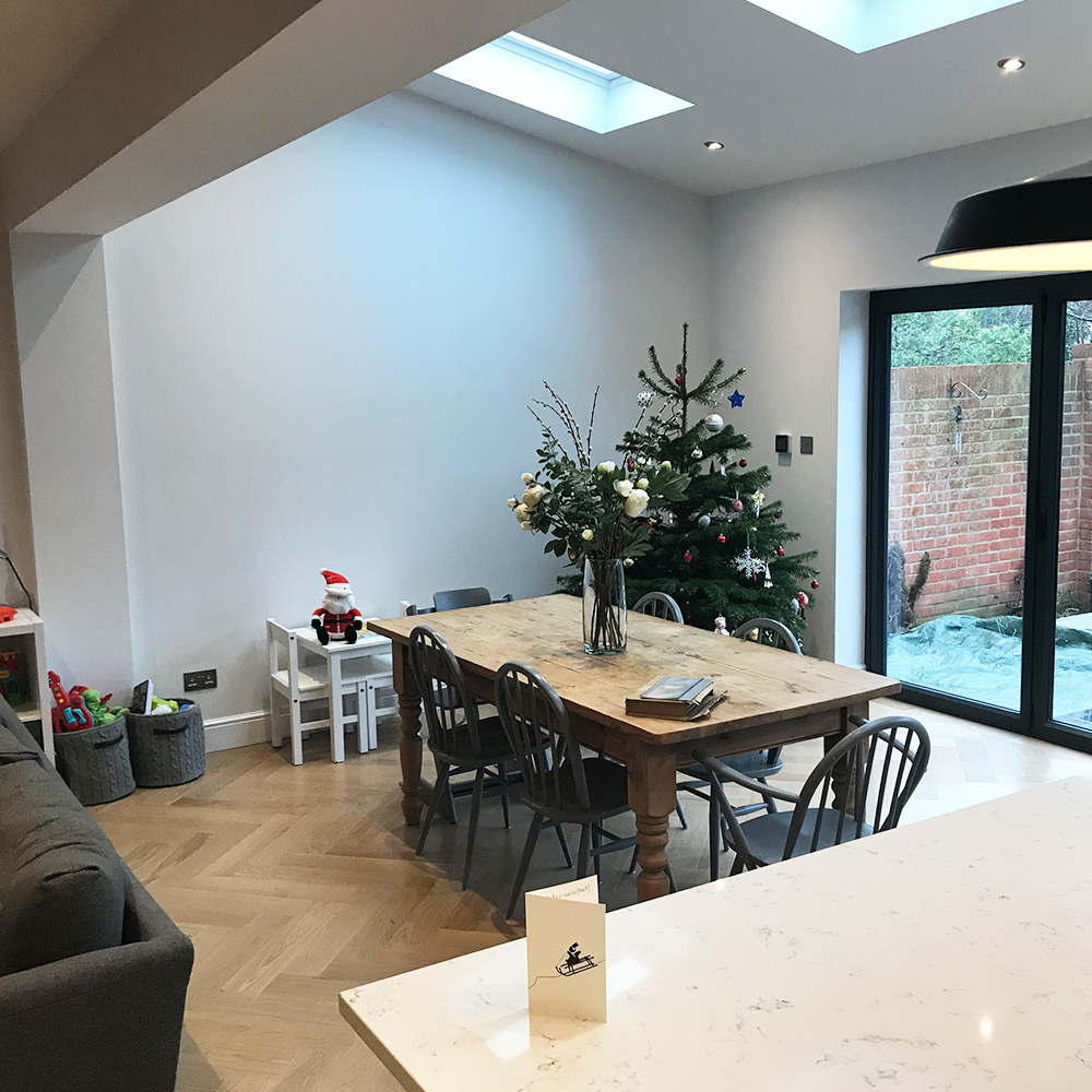A modern dining area with a wooden table, black chairs, a Christmas tree, and a skylight, next to glass doors leading to a patio.