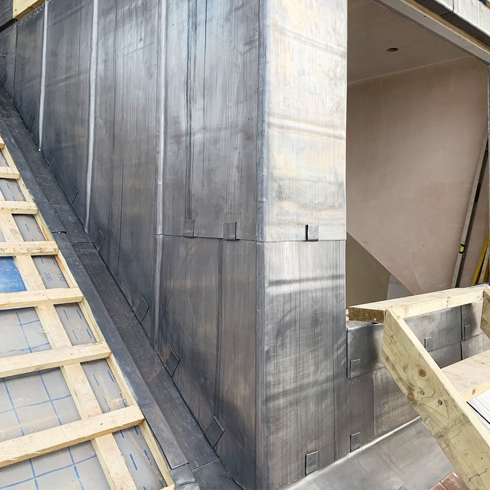 Close-up of a building under construction showing metal cladding on a wall and roof, with exposed timber framework and partially finished interior visible.